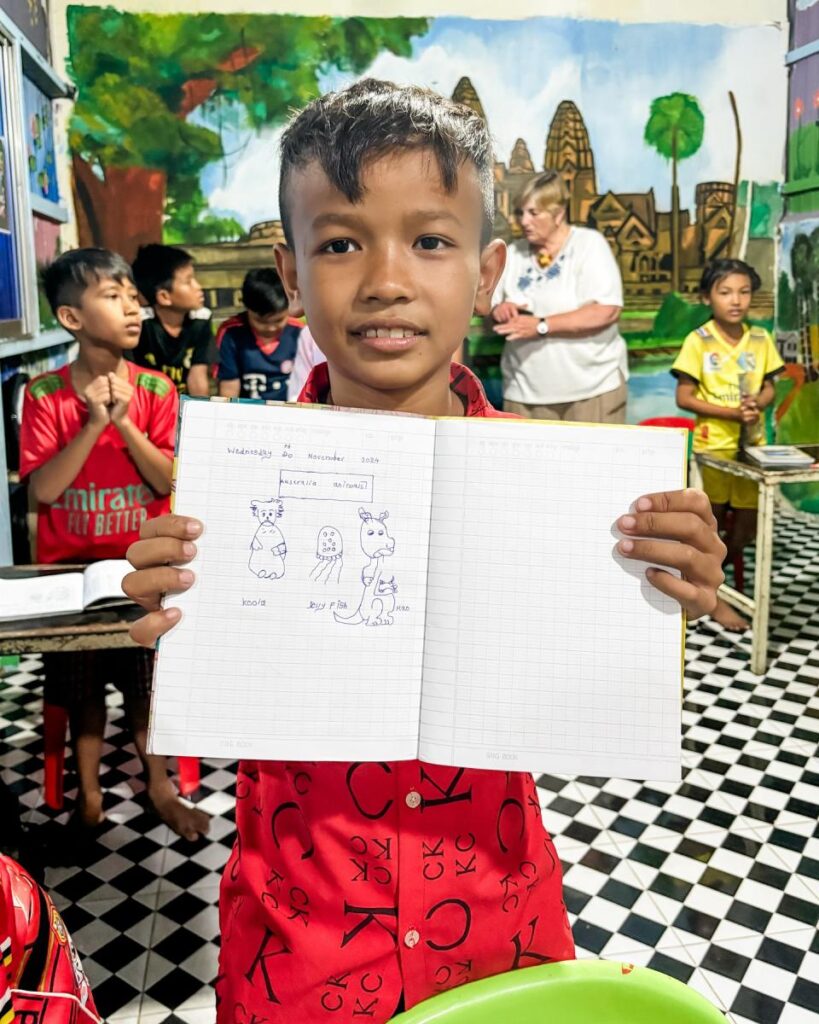 A DCC student proudly holding up his exercise book in the classroom